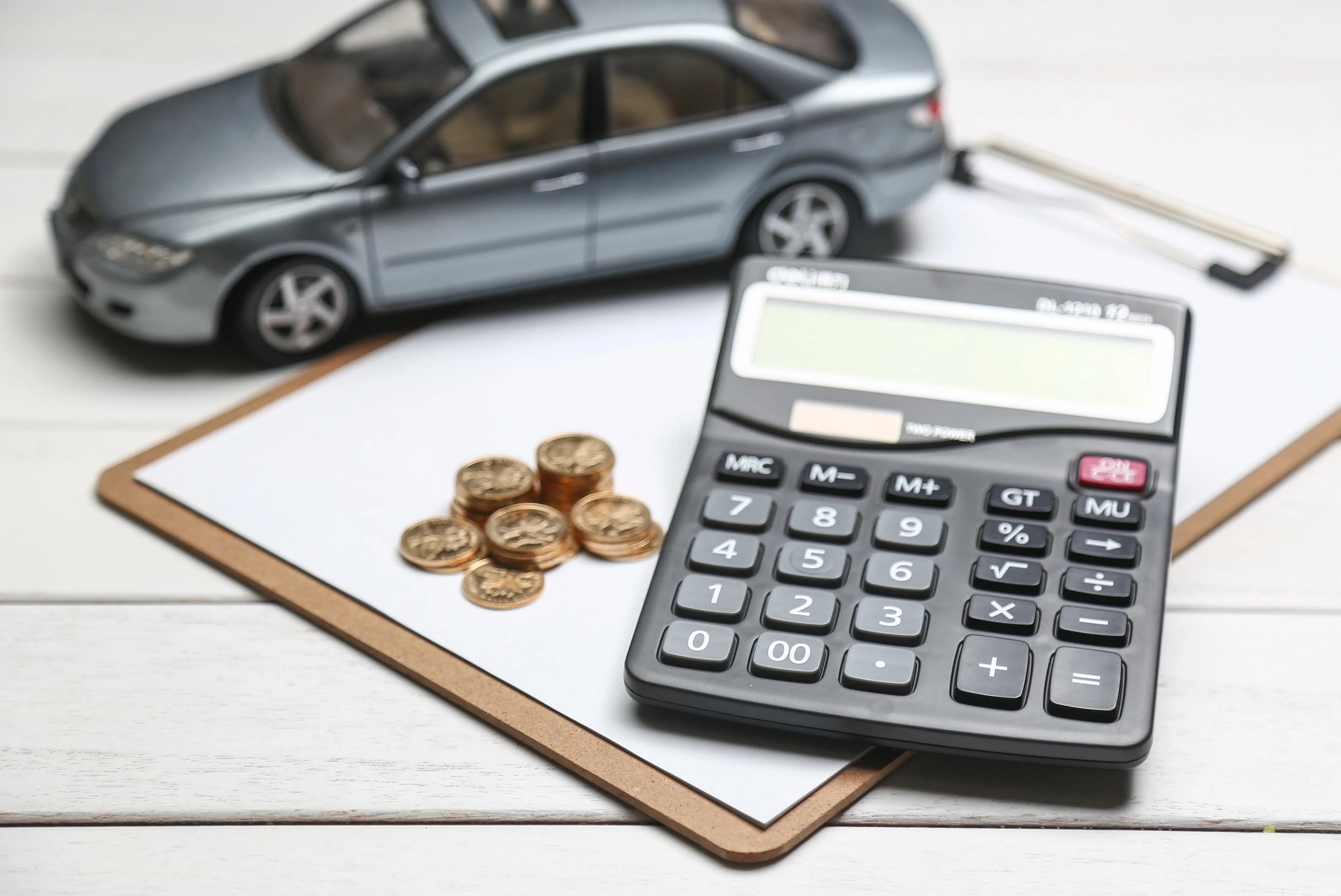 Car loan calculation setup with gray sedan model, calculator, coins, and clipboard on desk for automotive financing